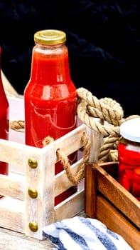 Glass jars with pickled red bell peppers and bottles with tomatoes sauce isolated in a rustic composition. Jars with variety of pickled vegetables preserved food concept.