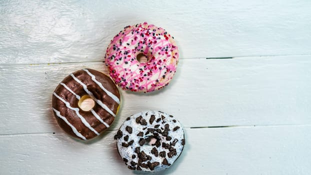 Colorful donuts on white wooden table. Sweet icing sugar food with glazed sprinkles, doughnut with frosting. Top view with copy space