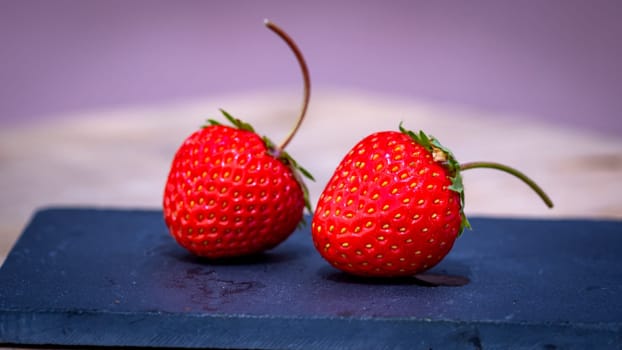 Close up of two strawberries on small black cutting board isolated outdoor on wooden table.