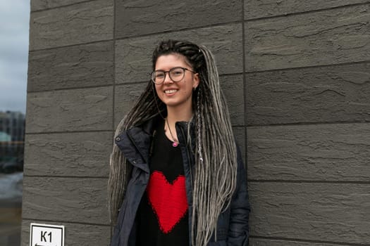 Photo on the street, young pretty informal woman with dreadlocks hairstyle smiling sweetly.