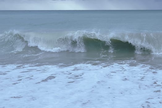 Waves breaking on the shore on small pebble beach. Storm clouds sky, turquoise water, waves,