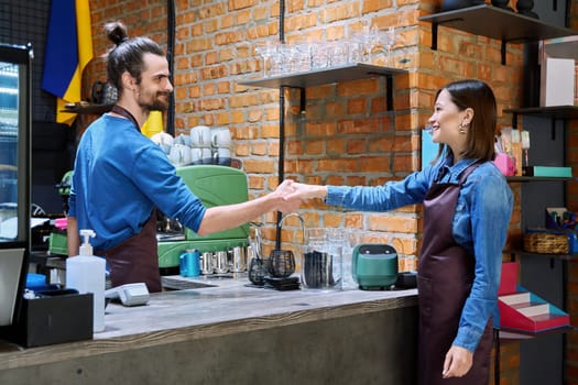 Colleagues, partners, young men and women in aprons shake hands in restaurant cafeteria coffee pastry shop. Cooperation, small business, partnership, teamwork, team, staff, friendship, success concept