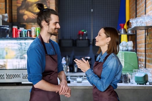 Small business team, successful colleagues partners workers young man and woman in aprons talking at workplace in restaurant coffee shop cafeteria. Cooperation, partnership, teamwork, staff, work