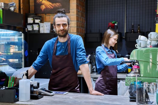 Business team colleagues partners young man woman in aprons working together in workplace behind counter in restaurant coffee shop cafeteria. Cooperation staff partnership teamwork work small business