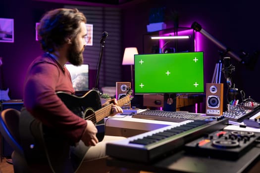 Artist learning to play guitar with internet lessons on greenscreen monitor, watching tutorials for acoustics rehearsal in home studio. Producer learns new string accords for music industry.