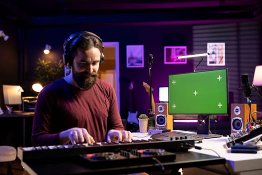 Audio engineer playing piano electronic keyboard notes in home studio, learning to play midi controller by watching tutorials on greenscreen pc. Musician hitting synthesizer keys for a song.