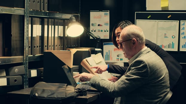 Investigation partners analyze archived autopsy reports and medical records for forensic insights, working in evidence room to gather clues. Law agents team confirm case details. Camera A.