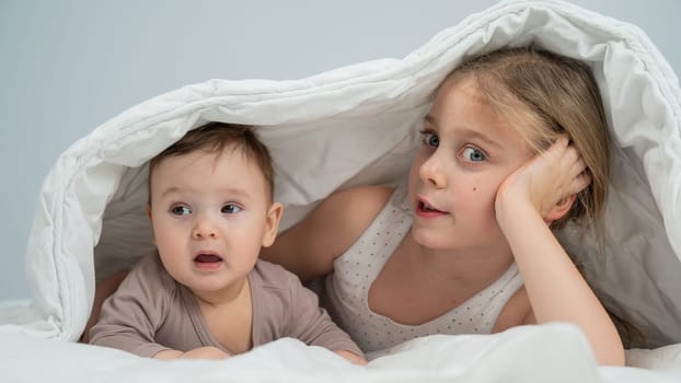 Little girl and her newborn brother hiding under the blanket