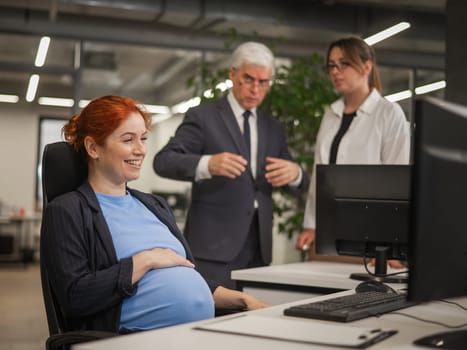 Happy Caucasian pregnant woman sitting at her desk, colleagues gossiping behind her back