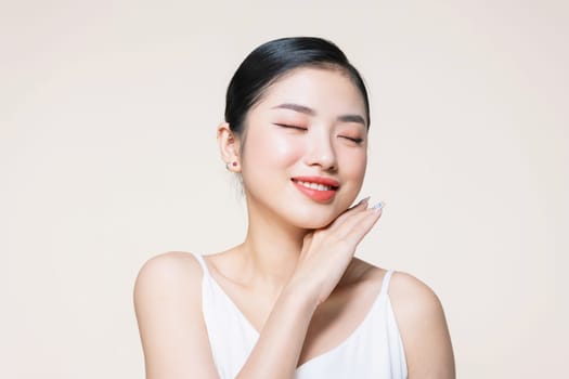 The beautiful Asian woman showing clear skin on the beige background.