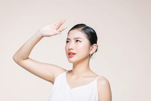 Woman covering her face from sun with her hand while standing against beige background