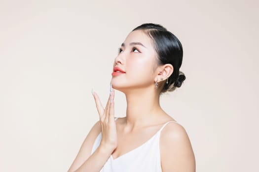 The beautiful Asian woman showing clear skin on the beige background.