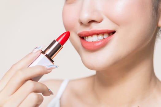 Young woman applying lipstick on beige