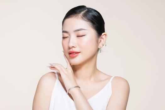 Young gorgeous asian woman touches her jaw line on beige background.