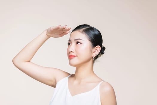Woman covering her face from sun with her hand while standing against beige background