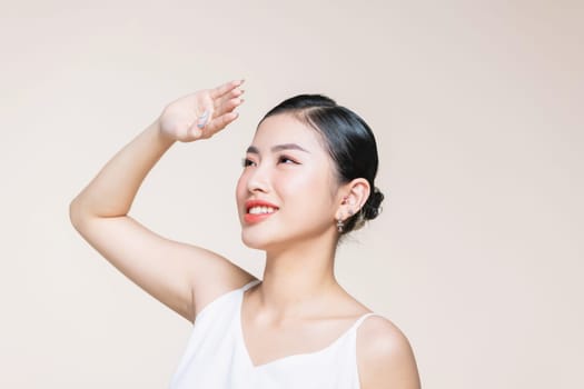 Beautiful young Asian woman raise arms to cover the sun with clean fresh skin on beige background.