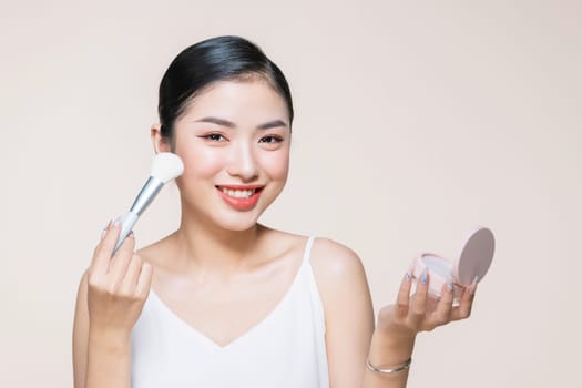 Portrait of attractive young adult woman applying blusher