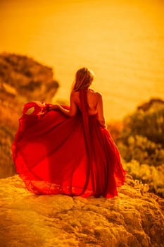 Woman sunset sea red dress, back view a happy beautiful sensual woman in a red long dress posing on a rock high above the sea on sunset