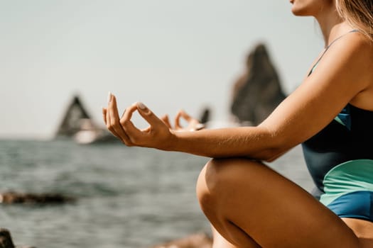 Yoga on the beach. A happy woman meditating in a yoga pose on the beach, surrounded by the ocean and rock mountains, promoting a healthy lifestyle outdoors in nature, and inspiring fitness concept