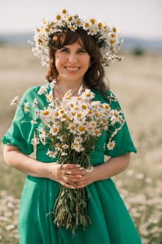 Happy woman in a field of daisies with a wreath of wildflowers on her head. woman in a green dress in a field of white flowers. Charming woman with a bouquet of daisies, tender summer photo.