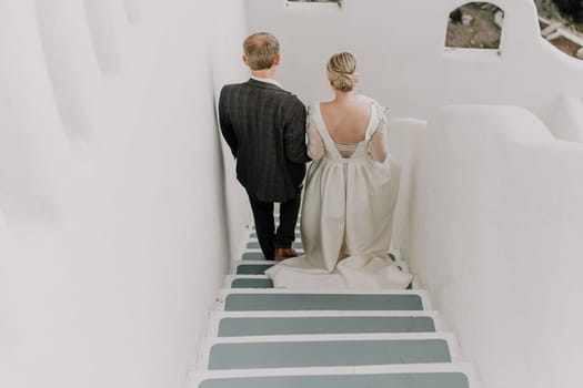 A bride and groom are walking down a white staircase. The bride is wearing a white dress and the groom is wearing a suit