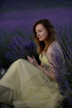 Woman poses in lavender field at sunset. Happy woman in yellow dress holds lavender bouquet. Aromatherapy concept, lavender oil, photo session in lavender.