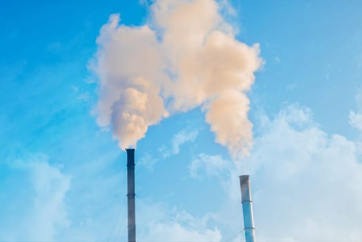 Two smoking factory chimneys against a blue sky. Increase CO2 and greenhouse gas emissions.