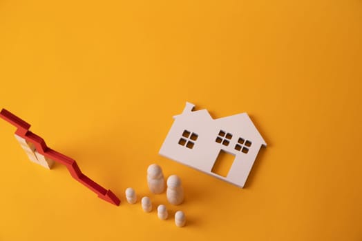 Wooden figurines of a family and a red down arrow next to a white house. The concept of reducing a housing loan to a young large family