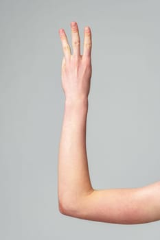 A human hand with fingers slightly apart is raised against a plain, neutral-colored background, signaling a nonverbal communication or waiting to be called upon.