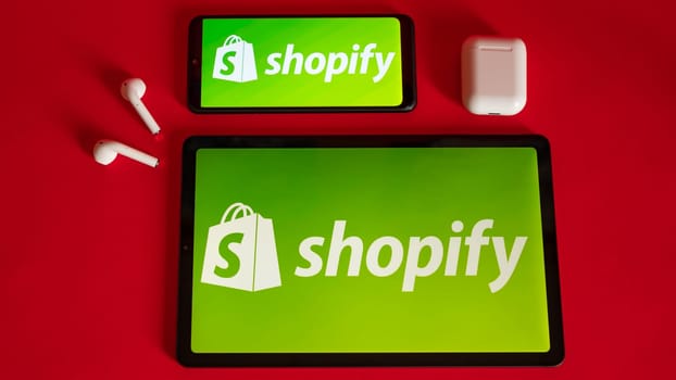 Tokio, Japan - June 05, 2022: Shopify web page displayed on a modern laptop, smartphone and notebook on red background. Shopify logo on iphone