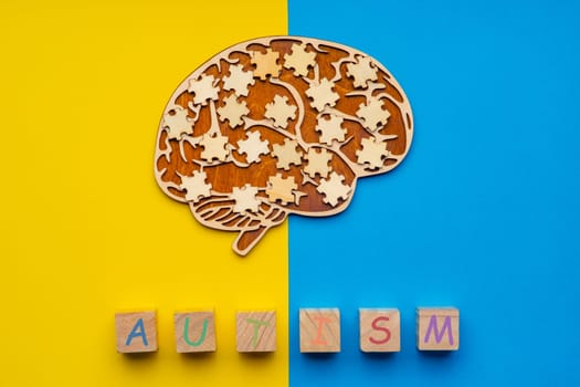 Mock up of a human brain with scattered puzzle pieces on a yellow and blue background. Six cubes with the inscription autism.