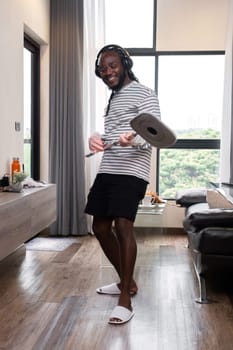 Happy young African American man doing housework, mopping floors, cleaning rooms on holiday, enjoying..