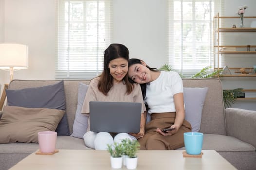 Mother and teenage daughter are looking at social media on laptop together on the sofa in the living room..