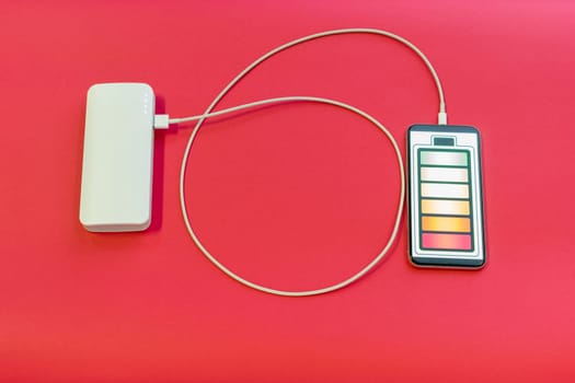 Smartphone is charging with power bank on red background - image