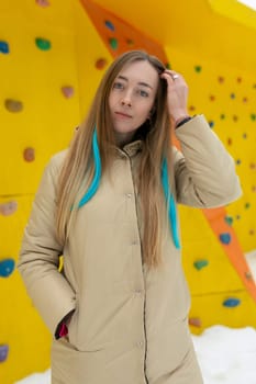 A woman with long hair stands confidently in front of a tall climbing wall, ready to tackle the challenging ascent ahead. She is focused and determined, her gear in place for a safe climb.
