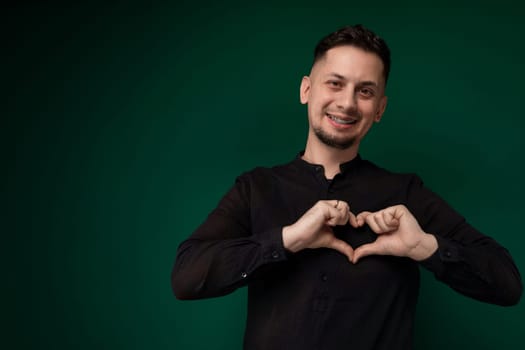 A man standing and forming a heart shape with his hands. His fingers are interlocked to create the symbol of love or affection. The background is simple, allowing the focus to remain on the hand gesture.