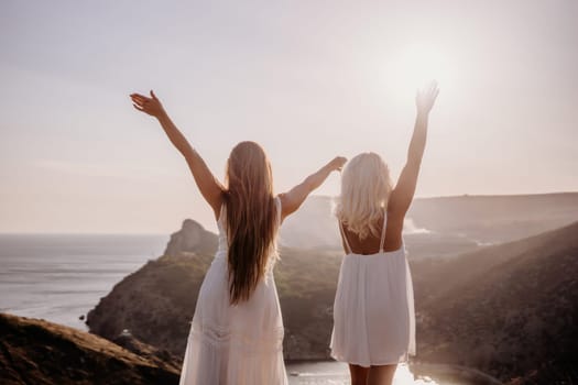 Two women are standing on a hill overlooking the ocean. They are holding hands and looking out at the water. The scene is peaceful and serene, with the sun shining brightly in the background