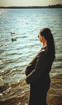 Pregnant brunette girl in sunglasses watching ducks