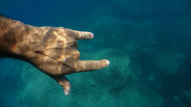 ily sign 3 fingers up human hand underwater detail close up