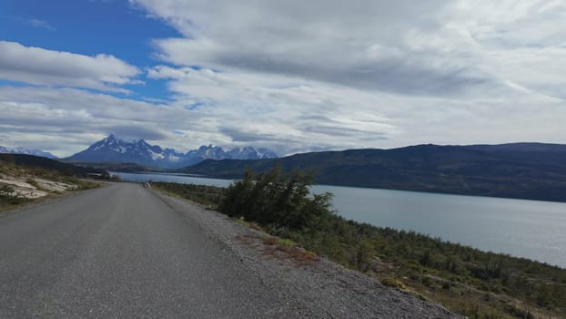 Driving towards Torres del Paine with a tranquil lake on the right, witnessing the rising grandeur of the mountain massif.