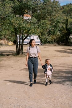 Mom and little girl walk holding hands through a green park. High quality photo