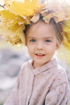 Small mysteriously smiling girl in a wreath of yellow leaves. Portrait. High quality photo