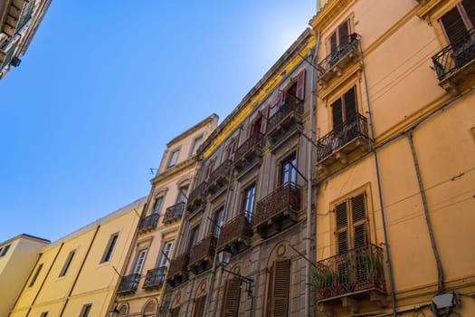 Cagliari historic center colorful buildings with wooden window shutters and iron balconies under clear blue sky in Sardinia Island, Italy.