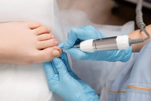 Pedicure master in rubber gloves making hardware pedicure using nail drill for woman.