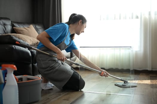 Professional cleaner in an apron cleaning floor in living room with mop. Cleaning service concept.