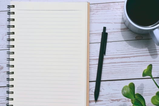 Top view of notepad and pen with cup of coffee on wooden desk. Copy space.