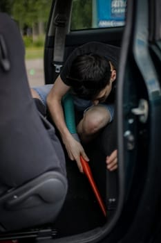 A handsome young caucasian brunette guy holds a tube with a nozzle in his hands and vacuums the seat in the car, side view close-up.