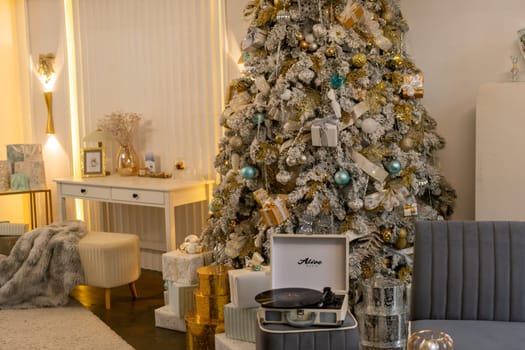 A Christmas tree with a record player on top of it. The room is decorated with presents and a white desk with a picture on it