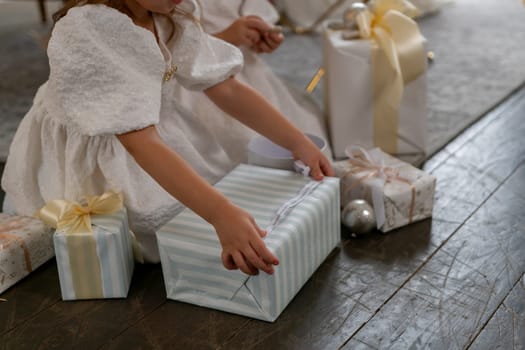 A young girl is opening a gift box with a ribbon on it. The scene is set in a room with a few other gift boxes and a bowl. Scene is joyful and festive