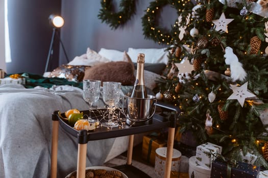 A Christmas tree with a champagne bottle and glasses on a tray. Scene is festive and celebratory